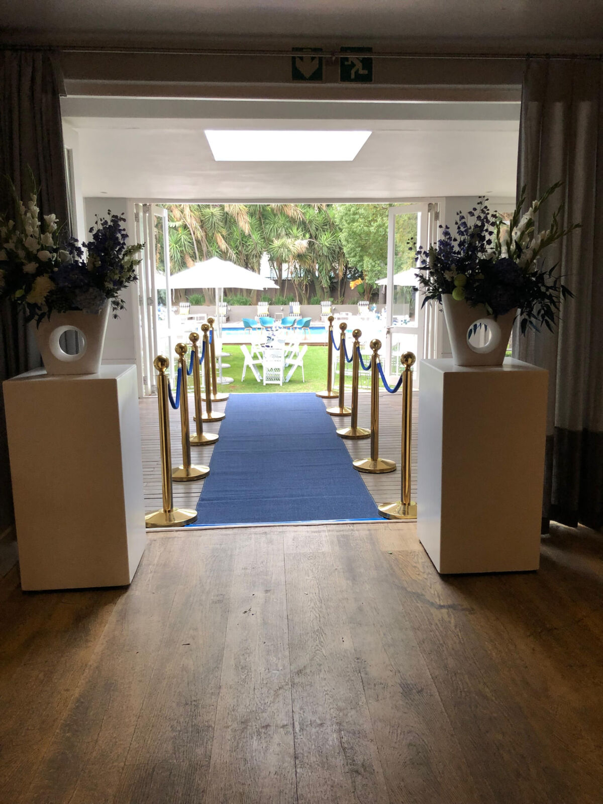 Blue carpet guest arrival with gold rope barriers and floral plinths